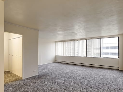 A room with a carpeted floor and a window with blinds.