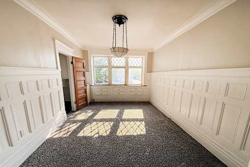 A room with white walls and a carpeted floor with a chandelier hanging from the ceiling.