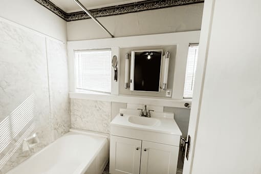 A white bathroom with a tub, sink, and mirror.