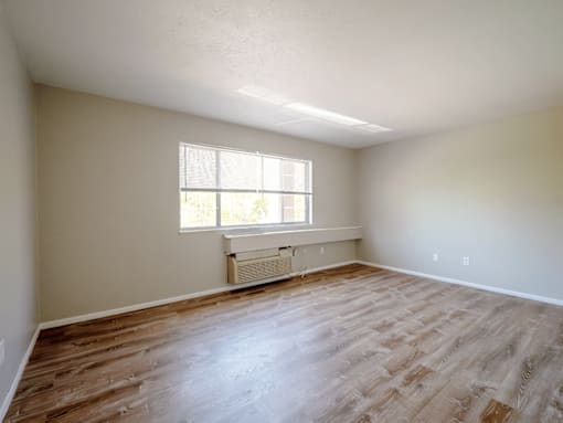 A room with wooden flooring and a window with blinds.