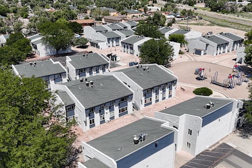 A large white building with a grey roof is surrounded by smaller white buildings with grey roofs.