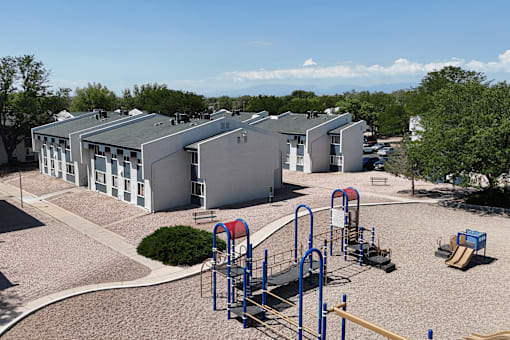 A playground with a slide, swings, and a monkey bars in front of a building.