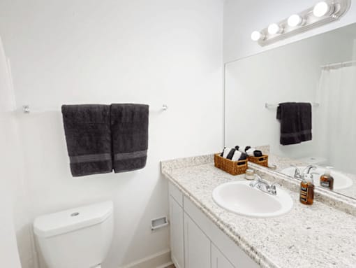 A bathroom with a toilet, sink, mirror, and towel.