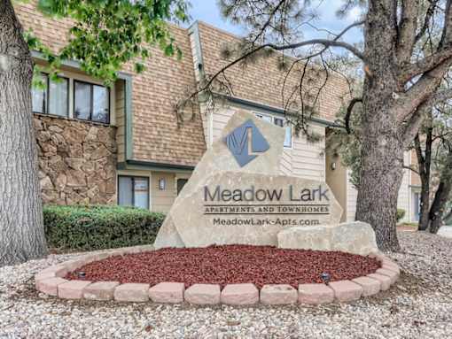 A sign for Meadow Lark Apartments and Townhomes stands in front of a building.