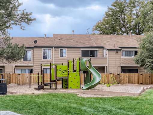 A playground with a yellow slide and a green slide in front of a building.