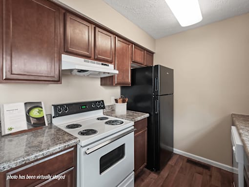 A kitchen with a black refrigerator, white stove, and brown cabinets.