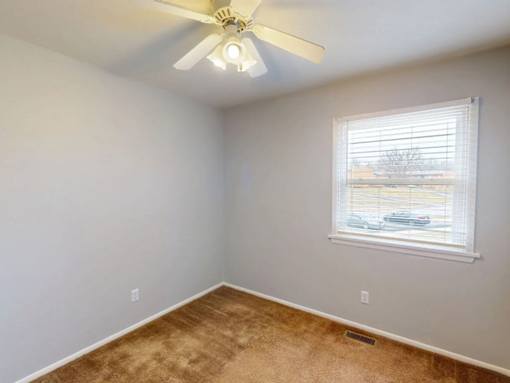 A room with a ceiling fan and a window with blinds.