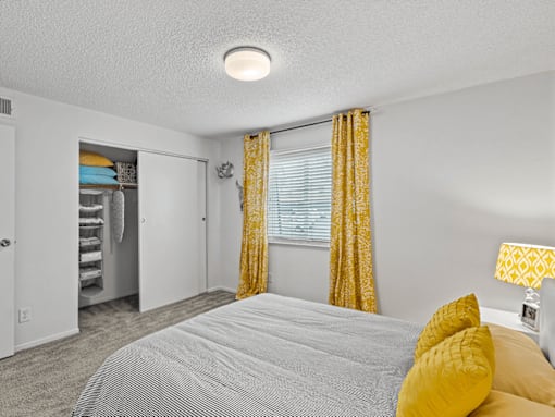 apartment bedroom with a bed and yellow curtains and a closet