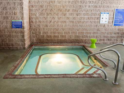 A small indoor pool with a brick wall and a metal ladder.
