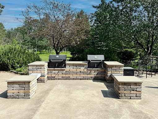A stone patio with two grills and a table.