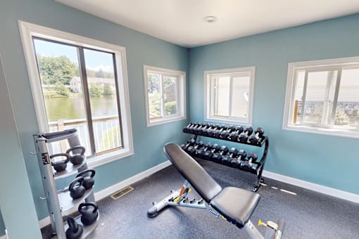 A room with a bench, weights, and windows.