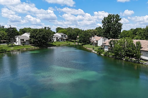 A lake surrounded by houses and trees under a blue sky.