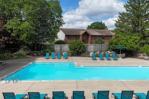 A pool surrounded by chairs and trees with a house in the background.