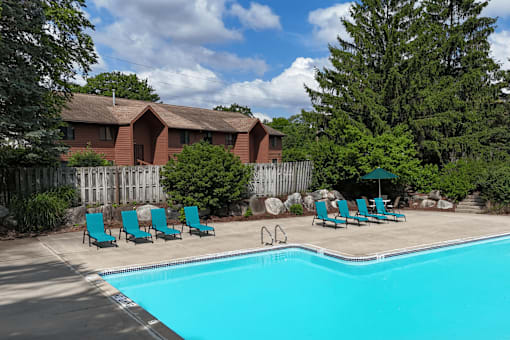 A pool with chairs and a house in the background.