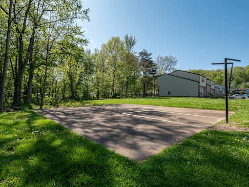 A paved area surrounded by trees and a building in the background.