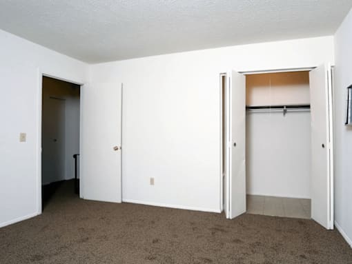A room with white walls and carpeted floor with a white door and a white closet with a white door.