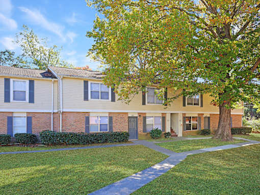 A tree with yellow leaves stands in front of a two-story apartment building.