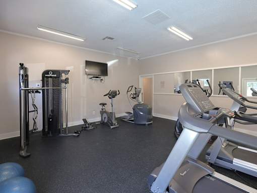 A spacious gym with treadmills, elliptical machines, and a television.