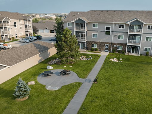 A large grassy area with a tree and a bench in front of apartment buildings.