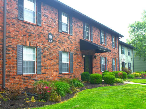 a brick apartment building with green grass and bushes in front of it