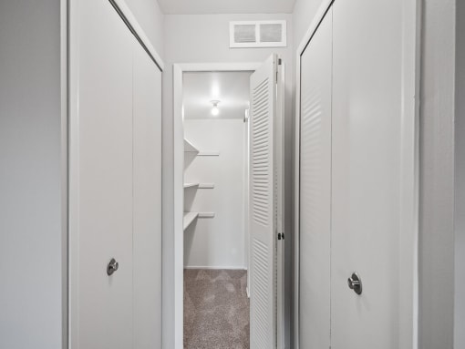 a closet in a small apartment with white doors and a white door to a bathroom