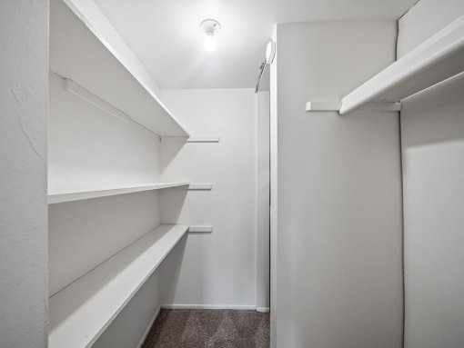 a walk in closet in a home with white walls and shelves