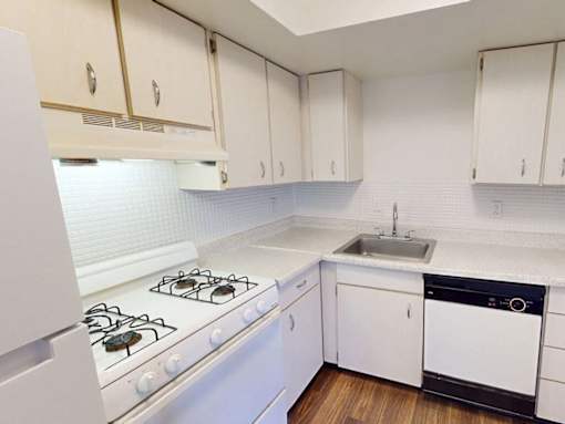 A white kitchen with a stove, sink, and cabinets.