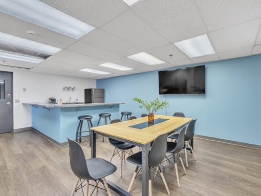 a conference room with a table and chairs with a kitchenette in the background