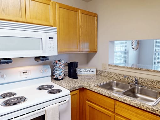 A kitchen with a white stove, wooden cabinets, and a granite countertop.