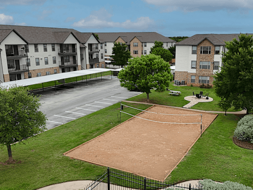 A tennis court is surrounded by apartment buildings.