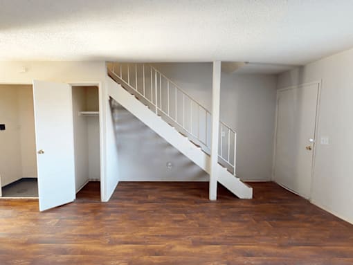 A white staircase with a railing is in the middle of a room with wooden floors.