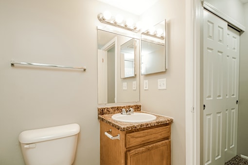 A bathroom with a toilet, sink, mirror and light.