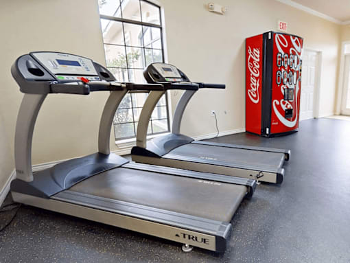 A Coca-Cola vending machine is in a room with treadmills.