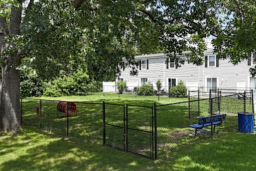 A black fence surrounds a green lawn with a blue bench and a red barrel.