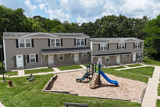 A playground area with a slide and a sandbox in front of a building.
