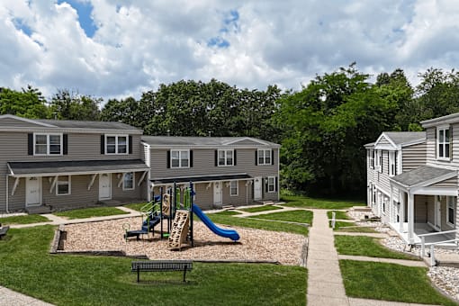 A playground with a slide and a bench in the foreground and apartment buildings in the background.