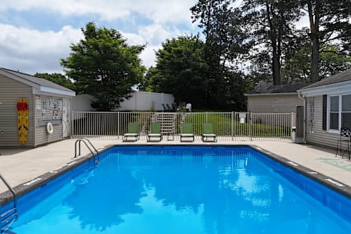 A small pool surrounded by a fence and chairs.