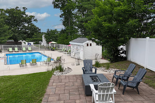 A backyard with a pool, patio furniture, and a white fence.