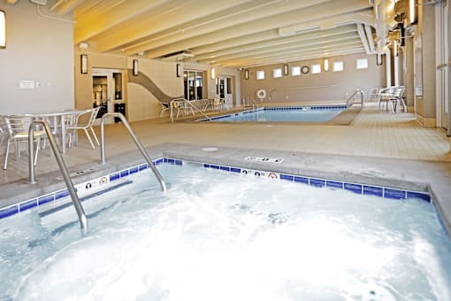 A hot tub in a room with a pool table and a staircase.