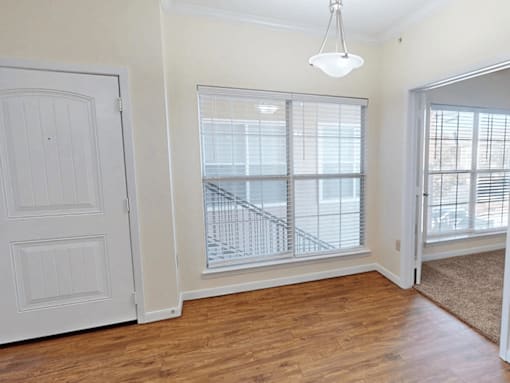 A room with a white door, a window with blinds, and a wooden floor.