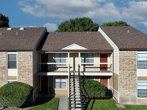 A two-story apartment building with a red door and a staircase leading to the second floor.