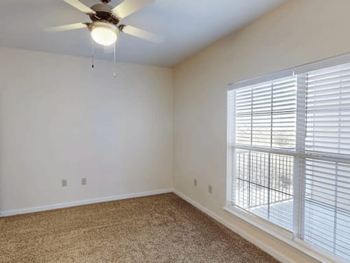 A room with a ceiling fan and a window with blinds.