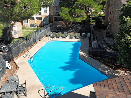 A blue swimming pool surrounded by a black fence and trees.