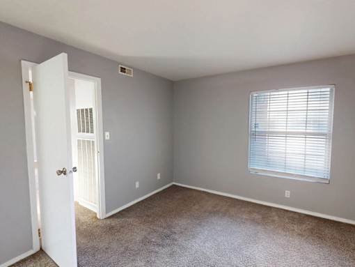A room with a carpeted floor and a window with blinds.