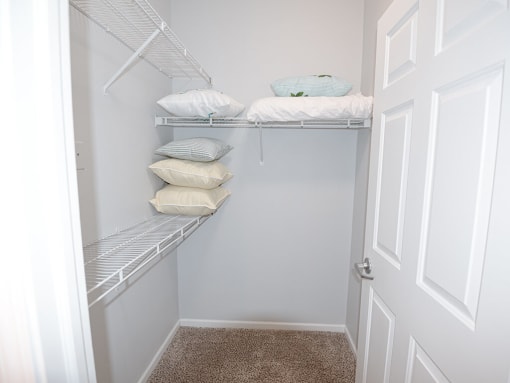 a walk in closet with white shelves and pillows