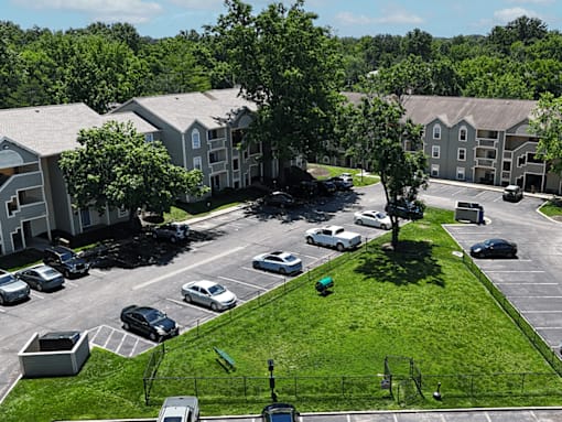 A dog park near a parking lot with cars and apartment buildings in the background.
