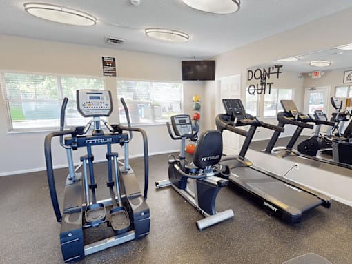 A gym with a row of treadmilers and elliptical machines.