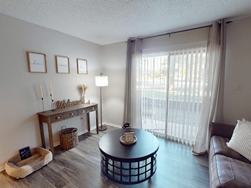 A living room with a brown leather couch, a round coffee table, and a dog bed.