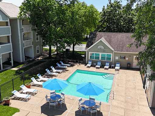 A pool surrounded by chairs and umbrellas with trees and a building in the background.