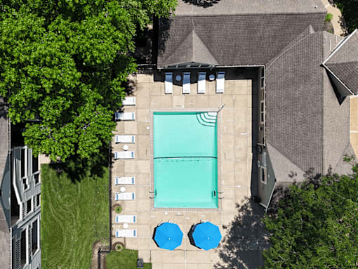 An aerial view of a swimming pool surrounded by trees and buildings.